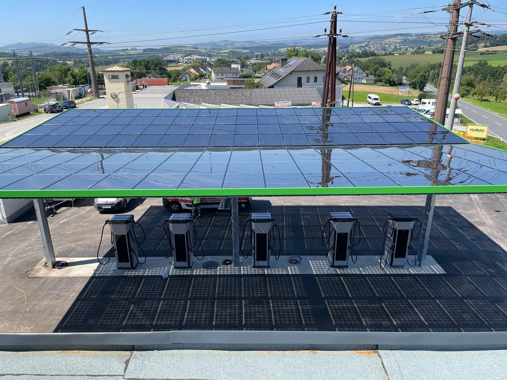 Bauphase: das Vordach von oben, fünf Säulen unter den Solarmodulen, dahinter Strommasten und Hügel