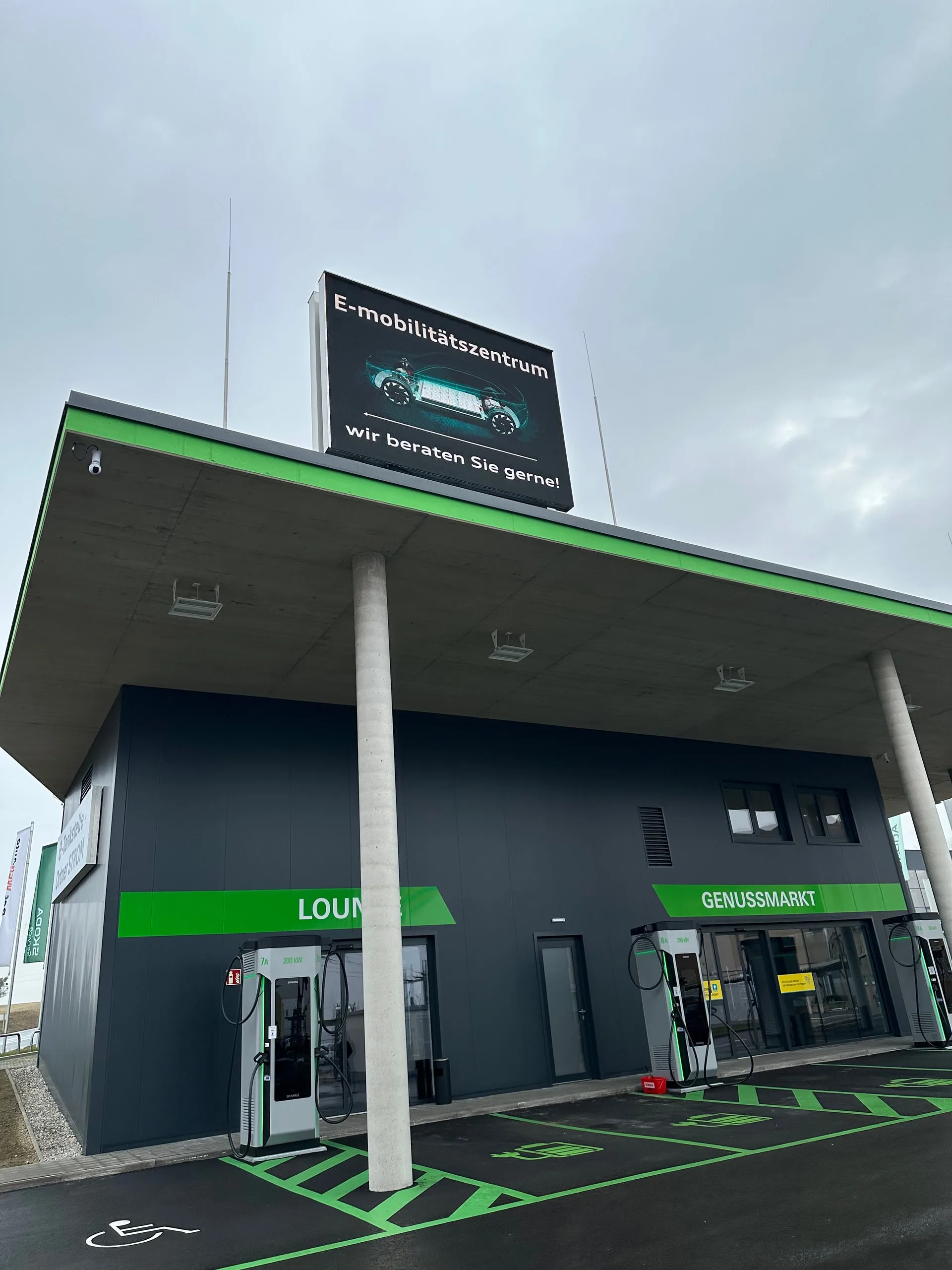 Gebäude am Ladepark mit Leuchtanzeige „E-Mobilitätszentrum, wir beraten Sie gerne“