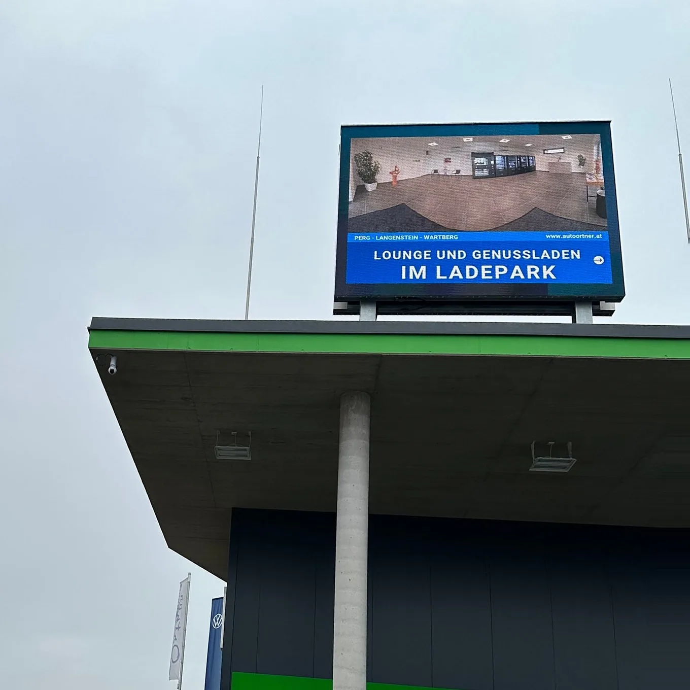 LED-Wand auf dem Vordach von Lounge und Genussmarkt, sie zeigt gerade Werbung für Lounge und Genussladen